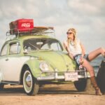 magia de lo retro, woman leaning on green and white Volkswagen Beetle near sea under white sky during daytime